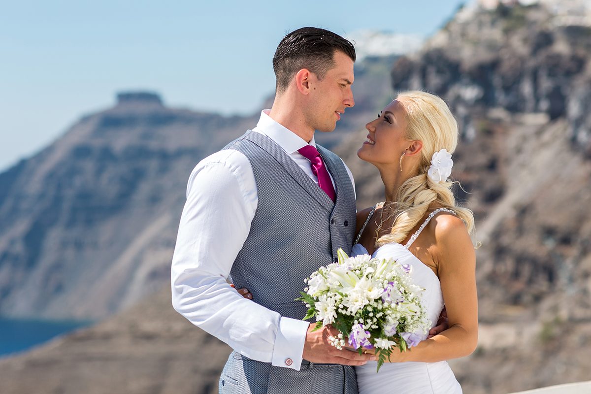 Couple smiling at each other against the Santorini caldera cliffs