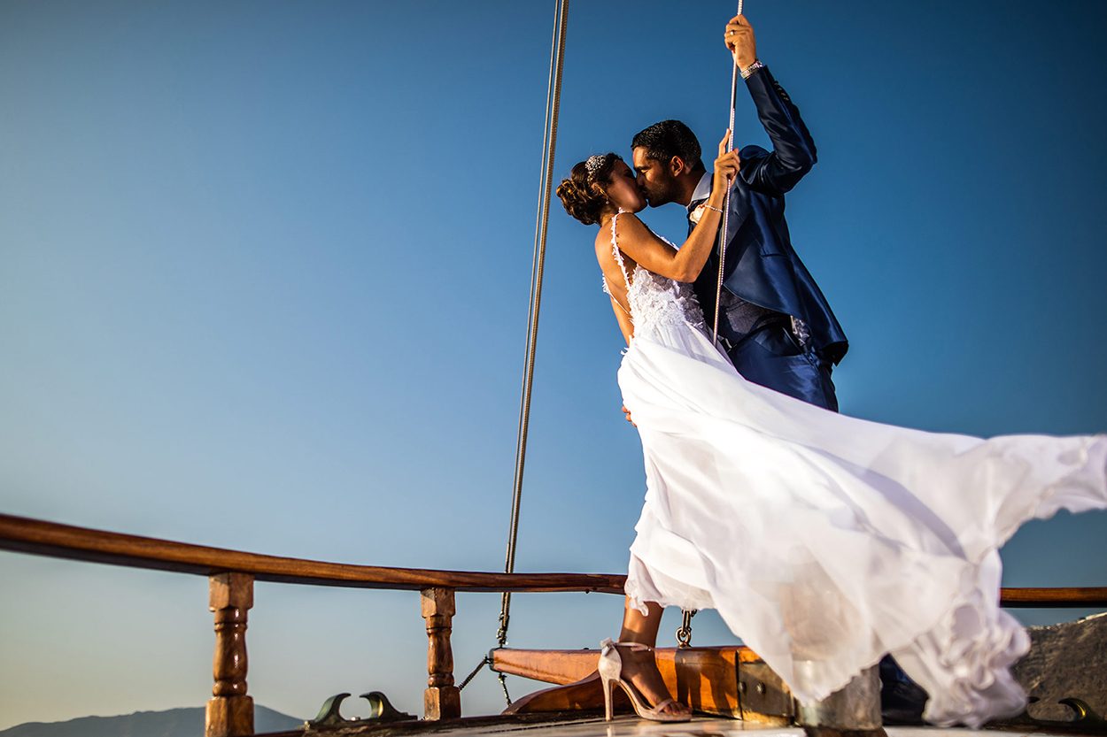 Bride and groom kissing on the deck of a boat beneath a deep blue Santorini sky