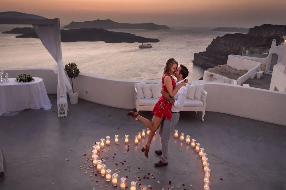 Marriage proposal at sunset on the Santorini caldera with candles arranged in a heart