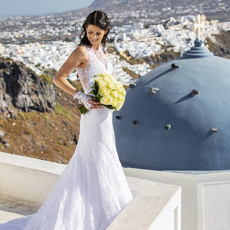 Bride with her bouquet beside the blue dome of Imerovigli in Santorini