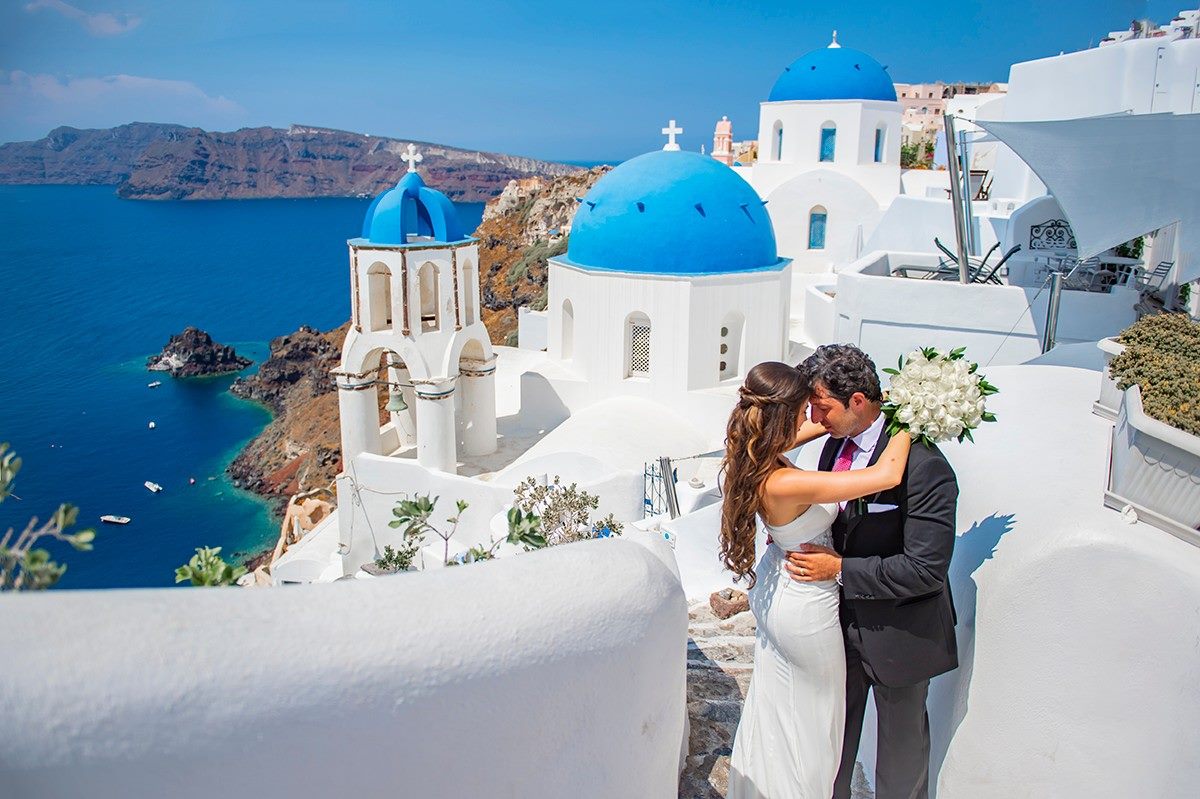 Bride and groom embracing above the blue domes of Oia, Santorini
