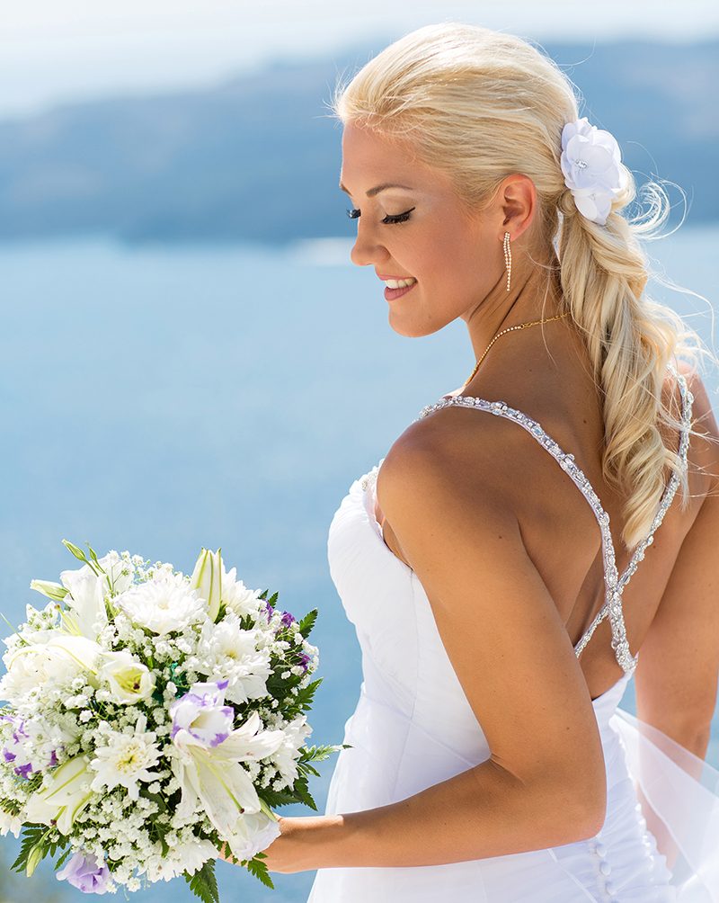 Bride with her bouquet above the deep blue Aegean in Santorini