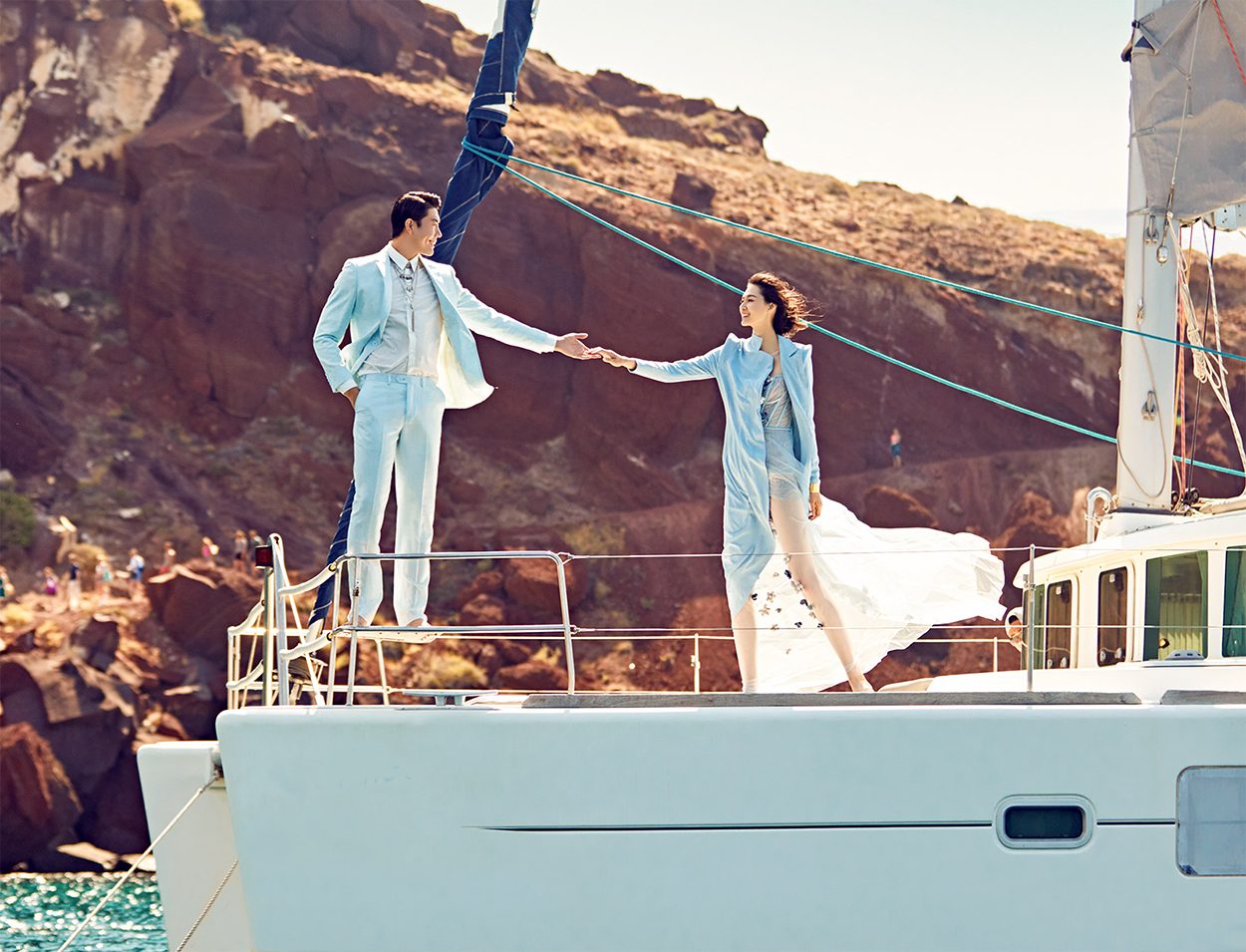 Couple holding hands on a catamaran beneath the red cliffs of Santorini
